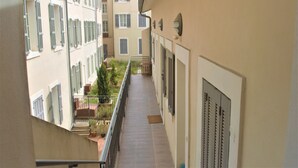 Un pasillo estrecho con balcones, plantas en macetas y vistas a edificios vecinos.