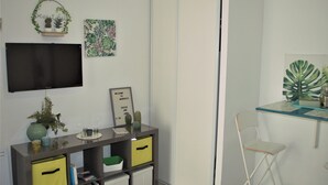 Una habitación con televisión en la pared, escritorio con ordenador, silla y planta.