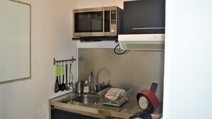 Una cocina compacta con microondas, pileta y escurridor.