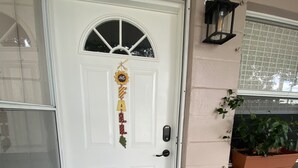 Une porte blanche avec une pancarte indiquant «Bienvenue», un paillasson avec un message et une plante en pot placée à côté de la porte.