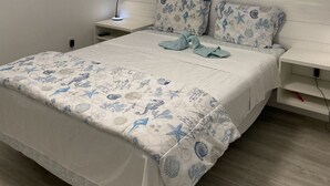 Une chambre à coucher comprenant un lit, deux tables de chevet, une commode, une étagère fixée au mur et une fenêtre avec des stores.