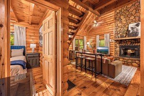 Move from the fireplace to the bar table without leaving the conversation. The open main floor keeps everyone together, with the bedrooms and loft stairs just beyond. - Hot Tub · Arcade Loft · Fire Pit · Wooded Cabin (Cherry Log)