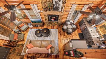 A log cabin interior with a fireplace, ceiling fans, a sofa, and a dining table.