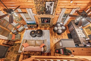 A log cabin interior with a fireplace, ceiling fans, a sofa, and a dining table. - Hot Tub · Arcade Loft · Fire Pit · Wooded Cabin (Cherry Log)