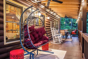 A log cabin with a hanging chair, outdoor seating, and a view of the forest. - Hot Tub · Arcade Loft · Fire Pit · Wooded Cabin (Cherry Log)