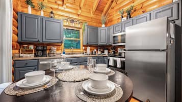 A modern kitchen with grey cabinets, a stainless steel refrigerator, and a dining table set for four.
