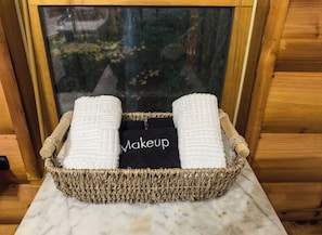 A wicker basket containing two white towels and a black towel with the word "Makeup" on it, placed on a marble surface. - Hot Tub · Arcade Loft · Fire Pit · Wooded Cabin (Cherry Log)
