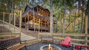 A cabin with a fire pit and Adirondack chairs in a forest setting. - Hot Tub · Arcade Loft · Fire Pit · Wooded Cabin (Cherry Log)