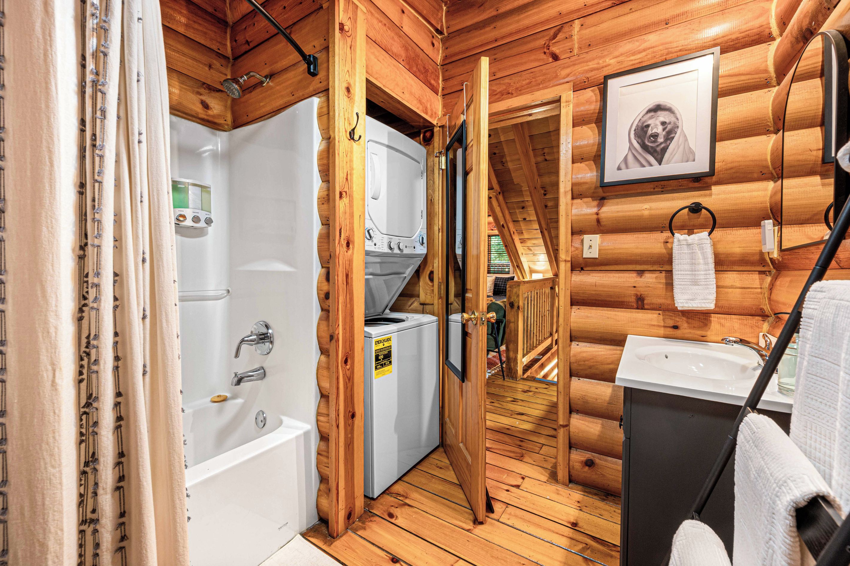Interior de una cabaña de madera con baño que incluye una bañera, lavadora y lavamanos.