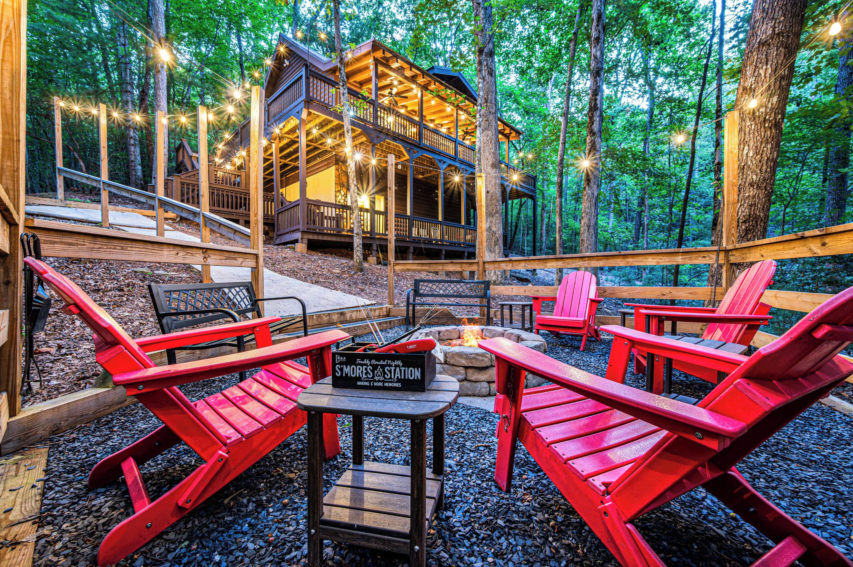 Gather the group around the fire pit and roast s'mores. The S'mores station is set out and ready, the trees close in around you, and the cabin sits up the hill.