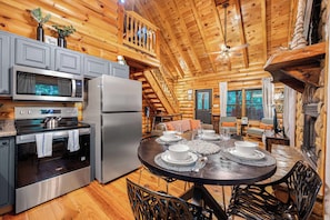 Cook dinner in the full kitchen with the whole group close by. Gas stove, fridge, dishwasher, and a table set for four just a few feet away. - Hot Tub · Arcade Loft · Fire Pit · Wooded Cabin (Cherry Log)