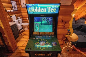 A Golden Tee arcade game in a cabin-style room with wooden walls and a wooden floor. - Hot Tub · Arcade Loft · Fire Pit · Wooded Cabin (Cherry Log)