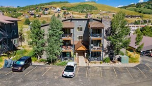 Un edificio de varios pisos con balcones, un estacionamiento y un paisaje montañoso al fondo.