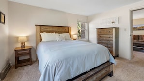 Un dormitorio con cama de madera, una mesita de noche con lámpara, un aparador y una ventana con vistas al exterior.