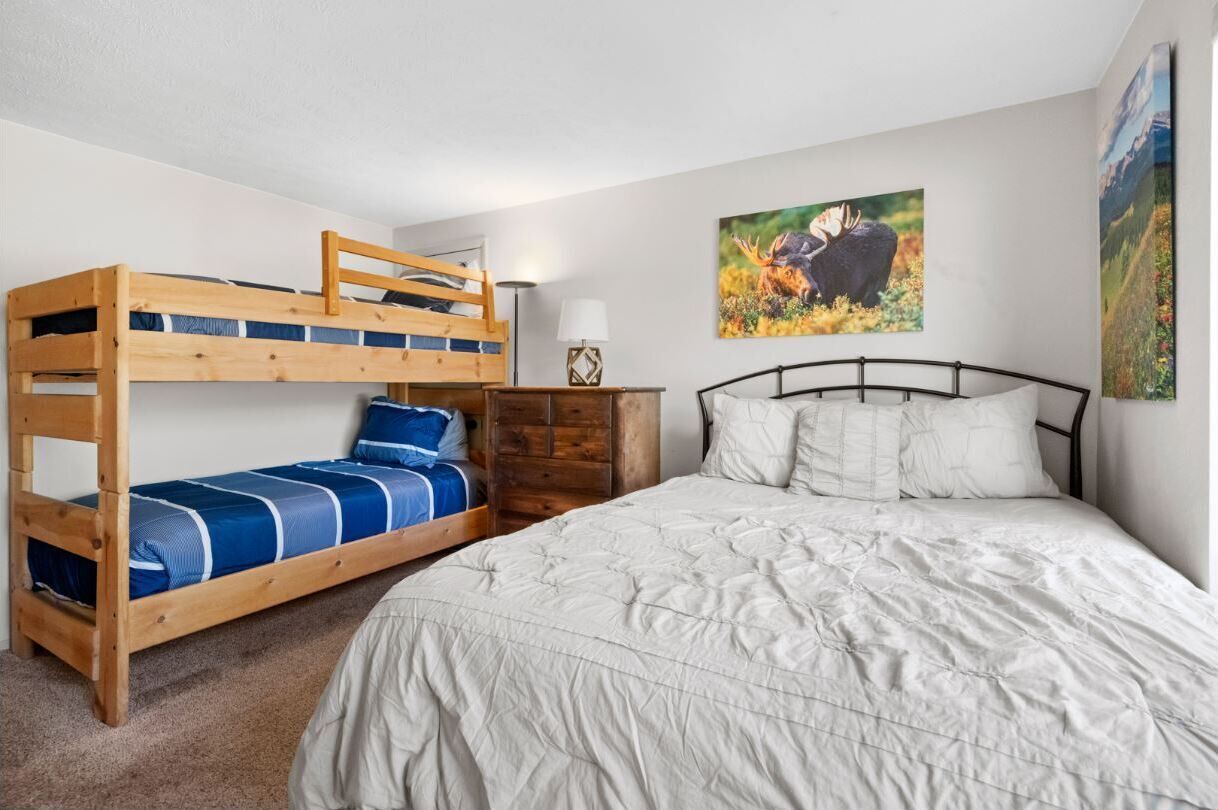 A bedroom with a bunk bed, a single bed, and a nightstand with a lamp.