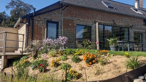 A brick house with a garden in front, a wooden deck, and a fenced area.