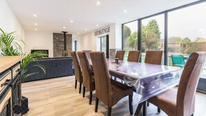 Een moderne eethoek met een grote tafel en stoelen, een accentmuur van natuursteen en grote ramen met uitzicht op de omgeving.