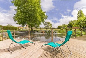 A wooden deck with two turquoise lounge chairs facing a pond, surrounded by greenery and a clear sky. - Gîte des 2 Amants (Flipou)