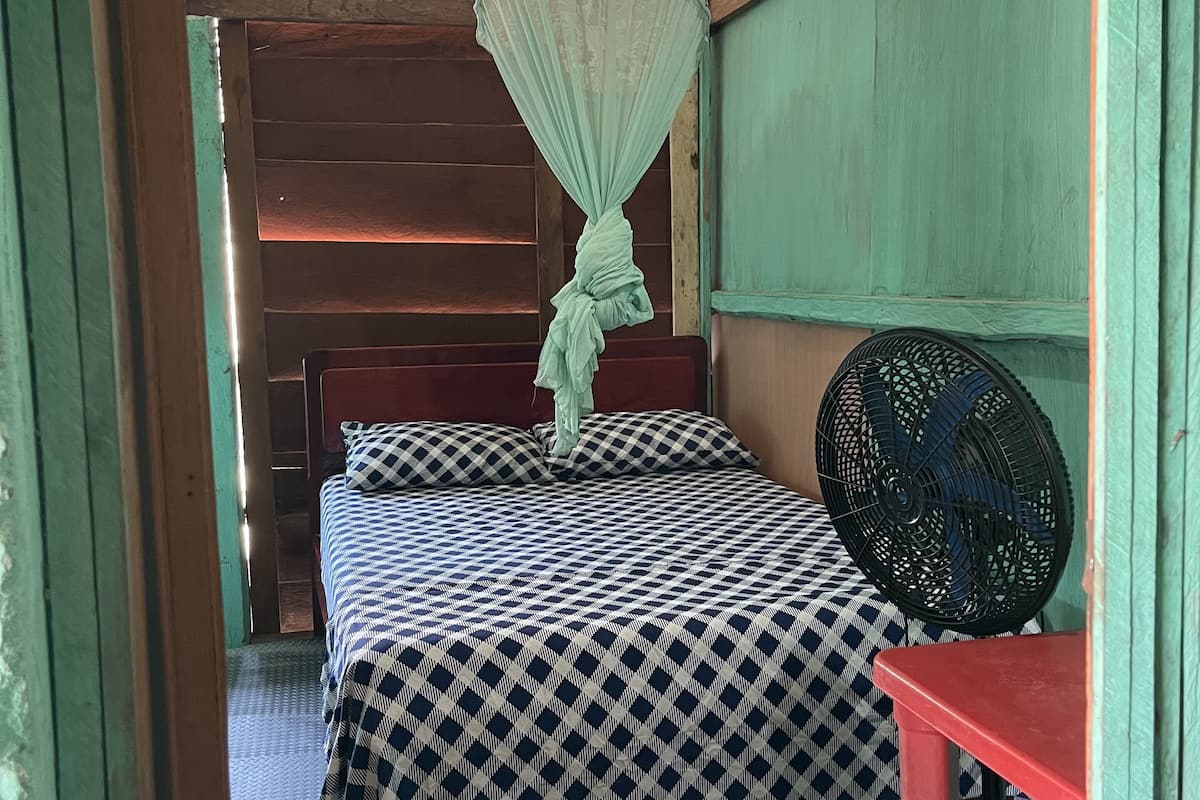 Ein Zimmer mit einem Bett, einem Ventilator und einem Moskitonetz.