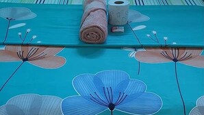 A bed with a teal floral bedspread, striped pillows, and a rolled towel. - Barra Zacapulco - Palapa Abrabam (Acapetahua)