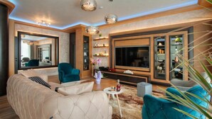 A modern living room with a large flat-screen TV, a beige sofa, teal armchairs, and a coffee table. - Villa Salute (Budva)