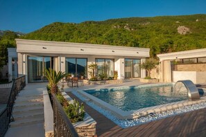 Une villa moderne dotée d’une piscine, d’un espace extérieur aménagé et offrant une vue sur un paysage montagneux.