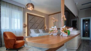 A modern hotel room with a large bed, a wooden console table, an orange armchair, and a TV. - Villa Salute (Budva)
