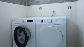A laundry room with two front-loading washing machines, a window, and a gray and white tiled backsplash. - Villa Salute (Budva)
