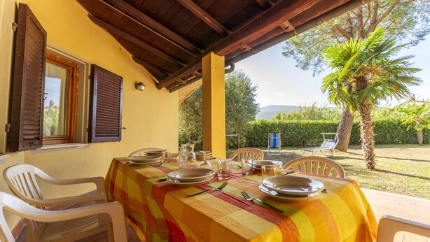 A dining area with a table set for four, covered with a striped tablecloth, surrounded by white plastic chairs. - Argentario Giannella Apartment (Orbetello)