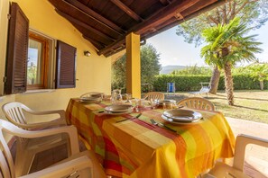 A dining area with a table set for four, covered with a striped tablecloth, surrounded by white plastic chairs. - Argentario Giannella Apartment (Orbetello)