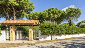 A gated entrance with a pergola, a white wall, and a large tree. - Argentario Giannella Apartment (Orbetello)