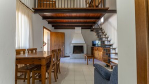 A spacious living area with a wooden dining table, chairs, a blue sofa, a fireplace, and a staircase leading to an upper level. - Argentario Giannella Apartment (Orbetello)