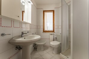 Kylpyhuone, jossa on pesuallas, kaksi wc:tä, peili ja ikkuna.