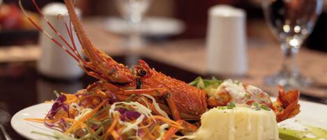A plate with a cooked lobster, a side salad, and a creamy dish, possibly a risotto or mashed potatoes, on a dining table.