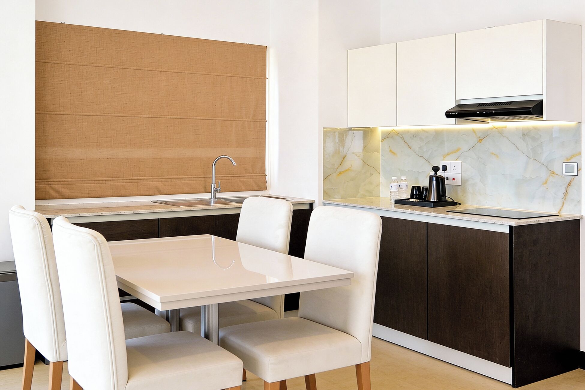 A compact kitchen with a white table and chairs, a built-in sink, and a coffee maker.