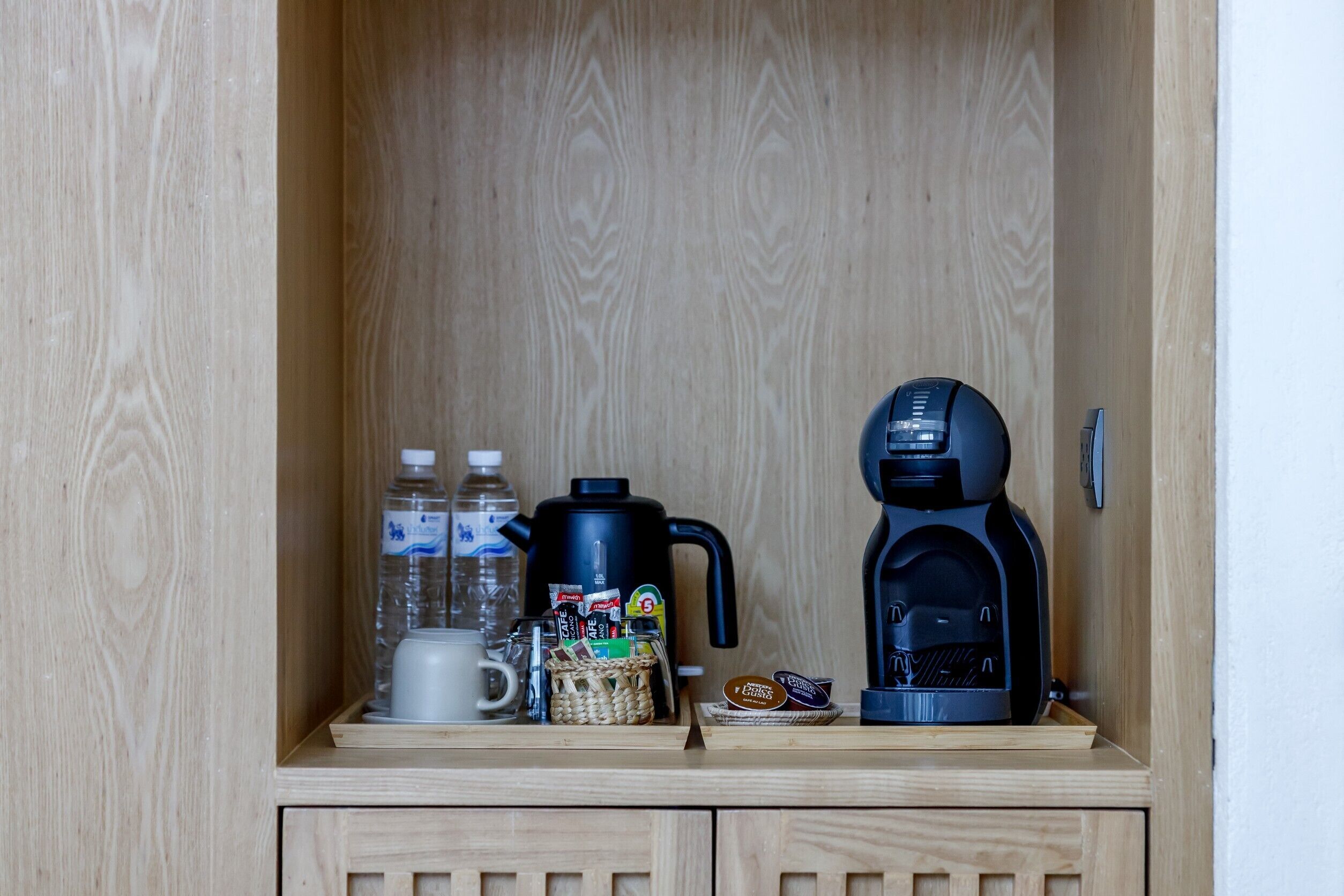 A wooden cabinet with a coffee maker, a water bottle, a mug, and a basket of snacks.