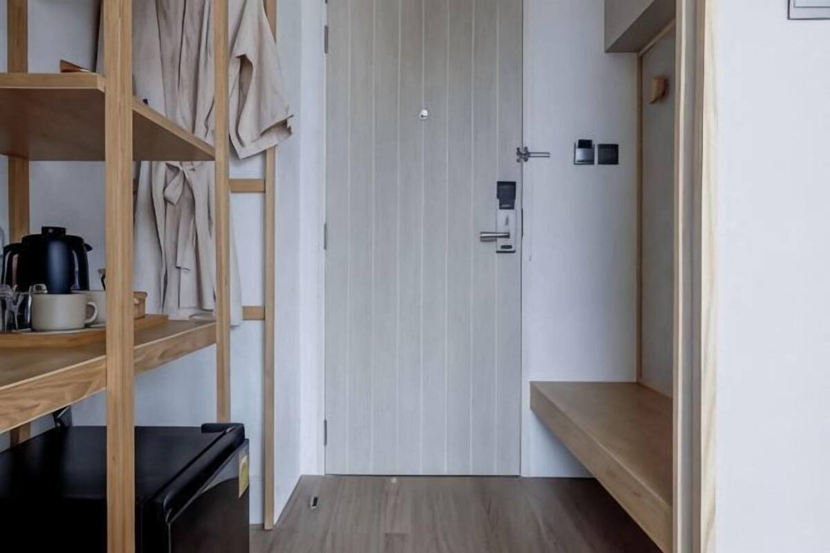 A room with a wooden shelf, a black appliance, a white door, and a small shelf with a kettle.