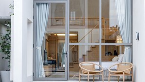 A modern room with a glass door, two wicker chairs, a bed, and a staircase leading to an upper level.