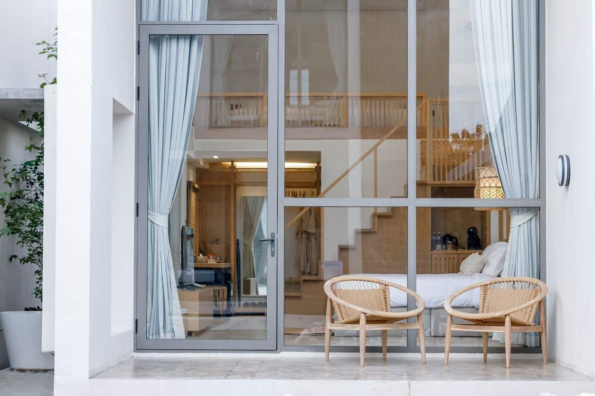 A modern room with a glass door, two wicker chairs, a bed, and a staircase leading to an upper level.