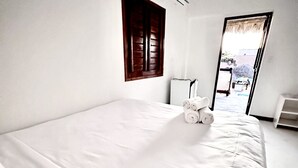 A clean, white room with a large bed, a window with wooden shutters, and a view of the outside. - Pousada VIGLAMO JERI (Jijoca de Jericoacoara)