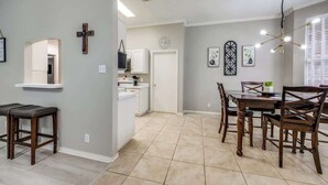 A dining area with a wooden table and chairs, a cross on the wall, and a kitchen in the background. - Spacious Brick House 3BR 2BA A+ (Denton)