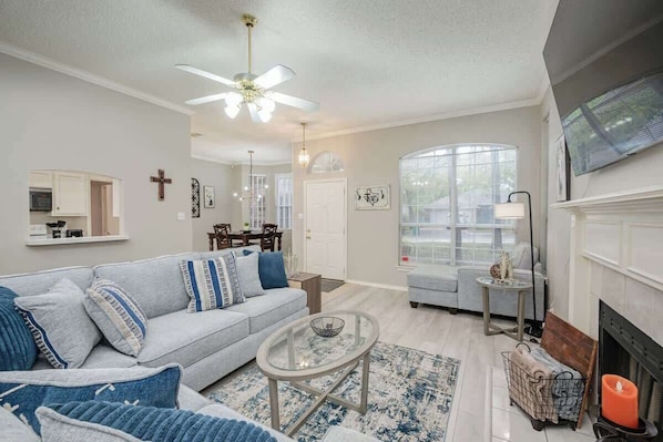 A living room with a sofa, coffee table, fireplace, and a television mounted on the wall.