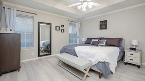 A bedroom with a bed, bedside table, nightstand, bench, ceiling fan, and a door. - Spacious Brick House 3BR 2BA A+ (Denton)