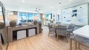 A spacious living area with a large window, a ceiling fan, and a dining table with chairs. - Beautiful Beach View Condo At Crystal Sands on Siesta Key! (Siesta Key)