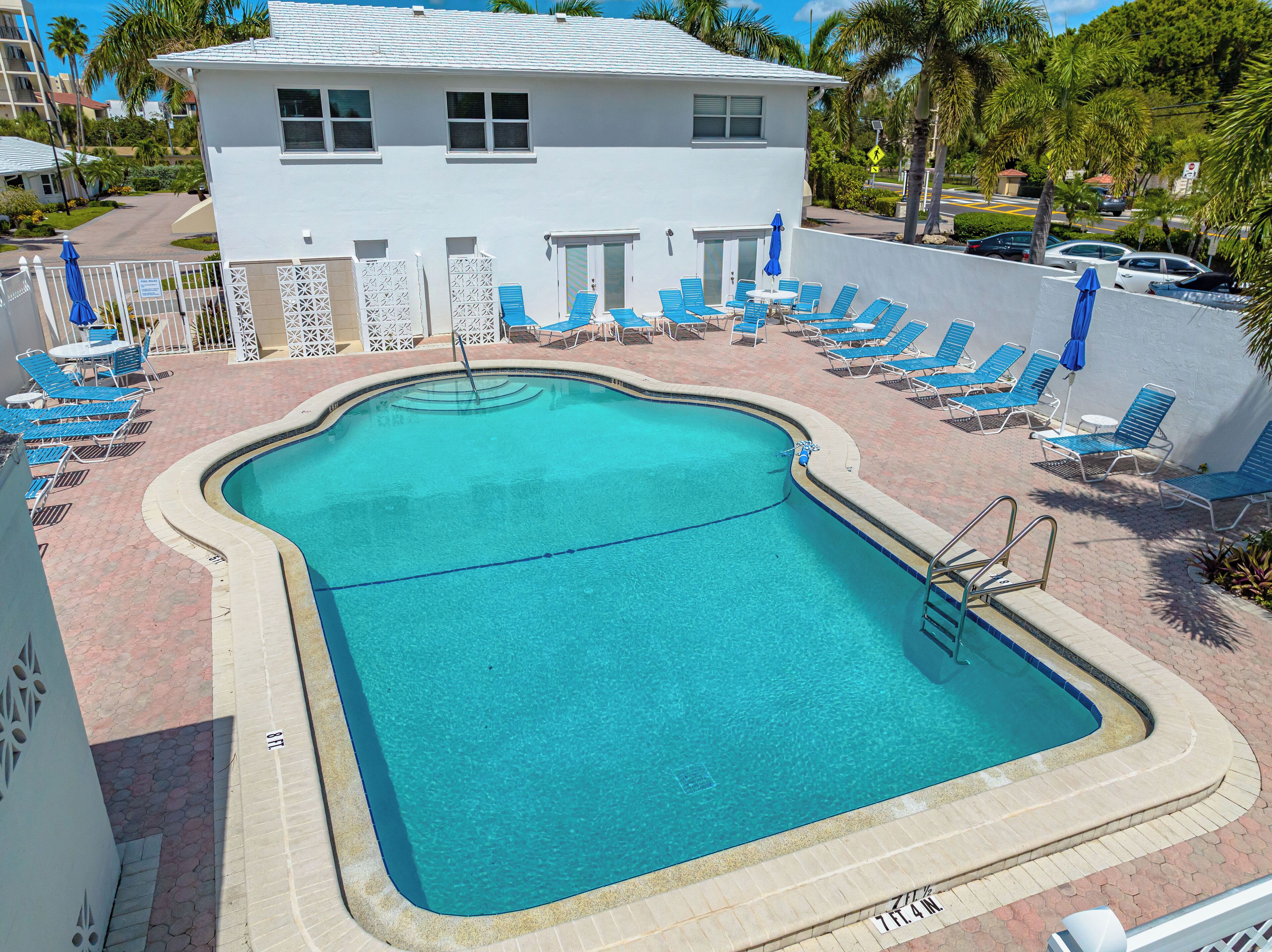 A swimming pool with a clear blue water, surrounded by blue lounge chairs and umbrellas, and a white building in the background.