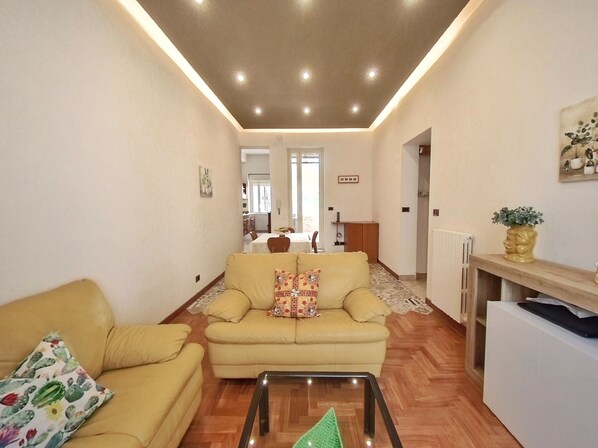 A living room with a sofa, a coffee table, and a dining area in the background.