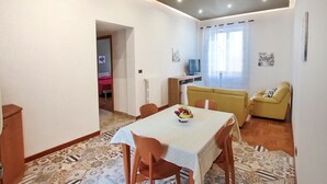 A dining area with a table and chairs, a sofa, a television, and a window with curtains. - Annacati House apartment, from 1 to 6 people, 3 bedrooms 2 bathrooms 1 terrace (Palermo)