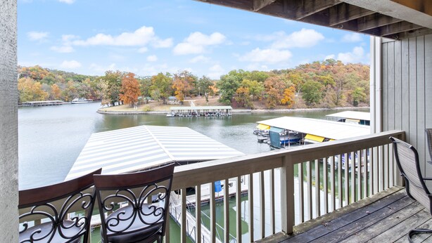 A wooden deck with a table and chairs overlooking a lake with boats and docks. - Central Location, Unlimited Indoor & Outdoor Fun (Osage Beach)