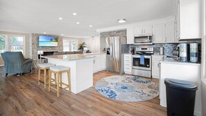 A modern kitchen with white cabinets, stainless steel appliances, and a central island with stools. - Two Homes, Large Deck, Firepit, Central Location (Sunrise Beach)