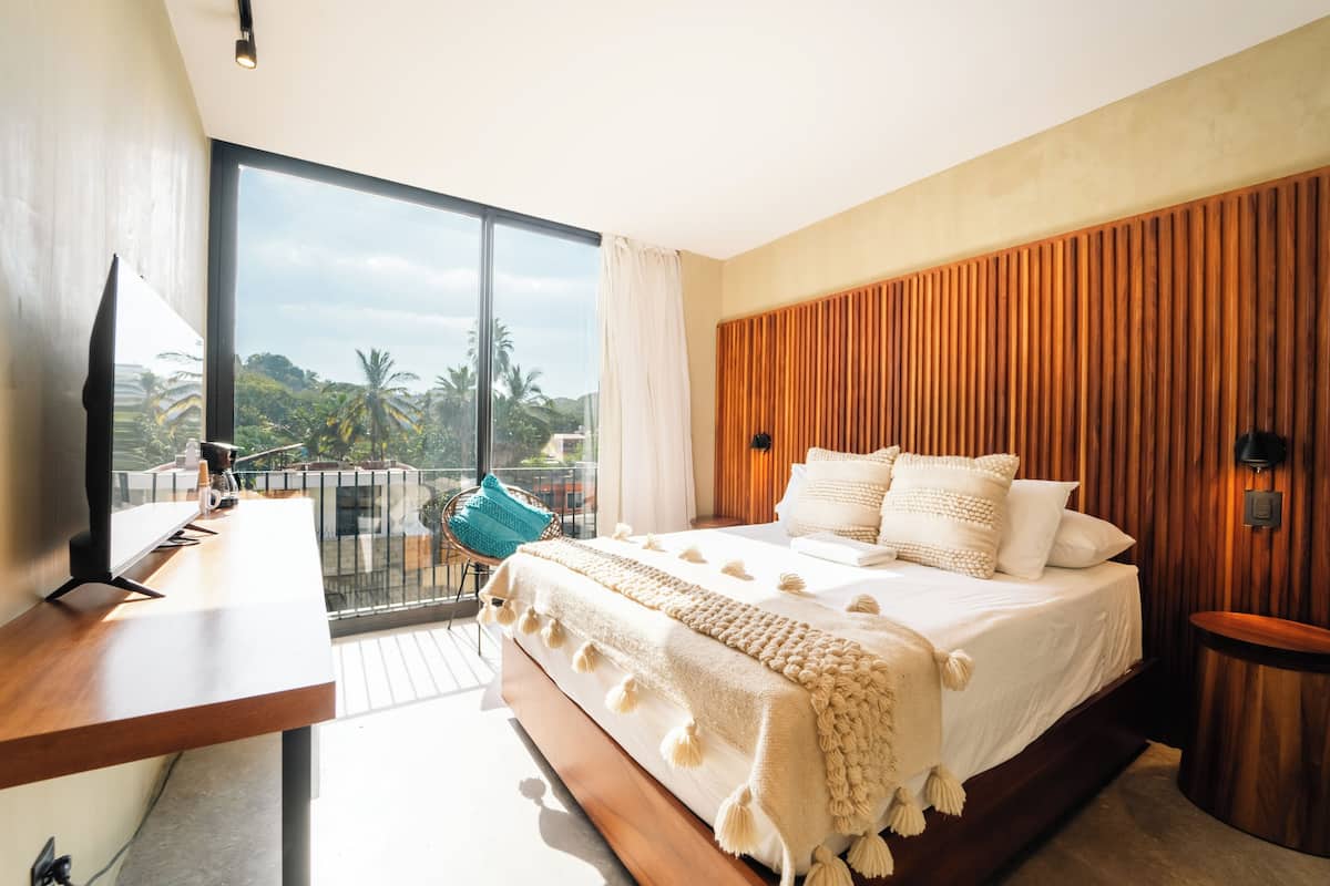 Une chambre moderne avec un grand lit, un bureau et un balcon offrant une vue sur les palmiers.